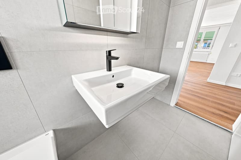 Modern bathroom with a white sink, sleek black faucet, large mirror with built-in cabinets, and grey tiled walls and floor.