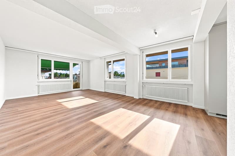 Empty room with wooden flooring, white walls, large windows, radiators, and a sliding glass door leading to a balcony.