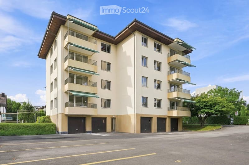 Multi-story residential building with balconies, garage, and parking area.