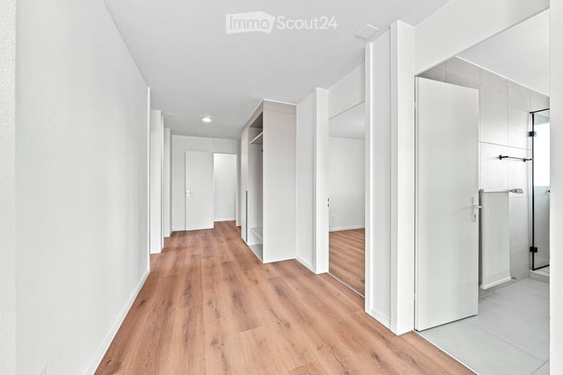 Modern, minimalist hallway with light wooden flooring, white walls, and several white doors leading to rooms.
