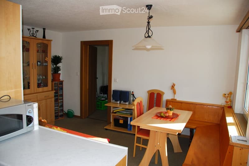 A cozy, well-furnished room with a microwave, wooden cabinet, dining table with chairs, a bench, and decorative items including a plant and candle holder.