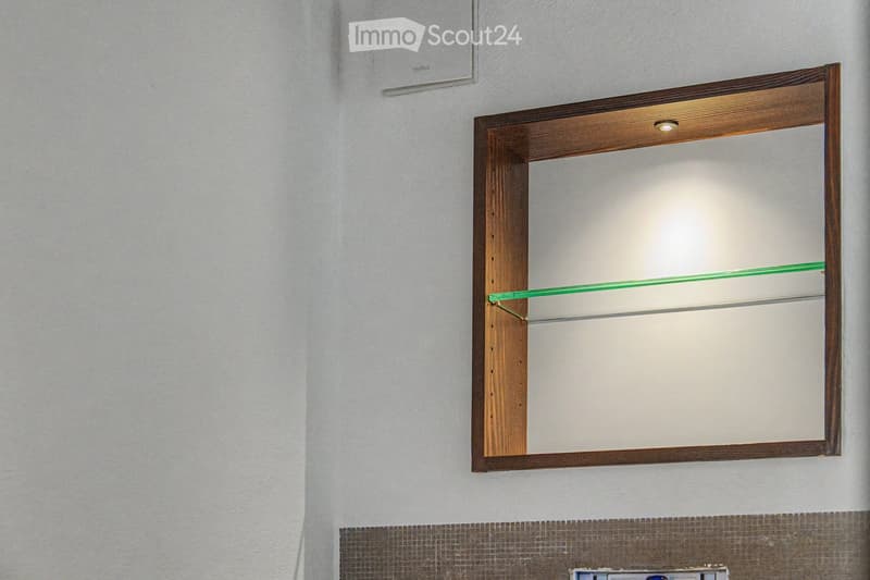 Bathroom with a wooden-framed mirror and built-in glass shelves, mounted on a light grey wall with a tiled lower section.