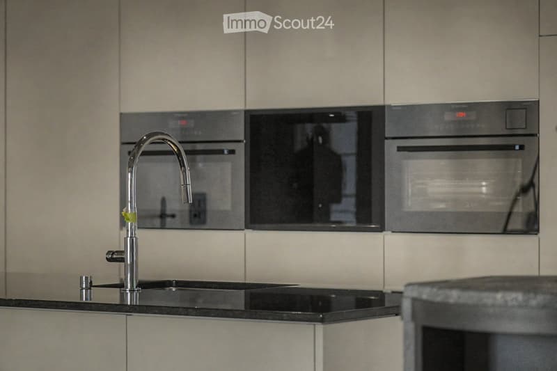 Modern kitchen with sleek, light-colored cabinets, a black countertop, a contemporary faucet, and built-in ovens.
