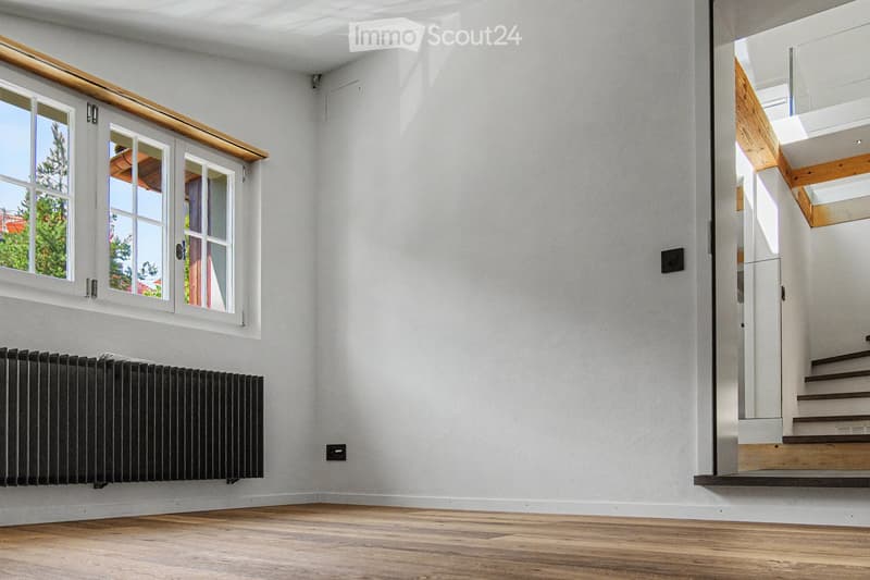 Empty room with light-colored walls, wooden flooring, a radiator, and a staircase leading upwards.