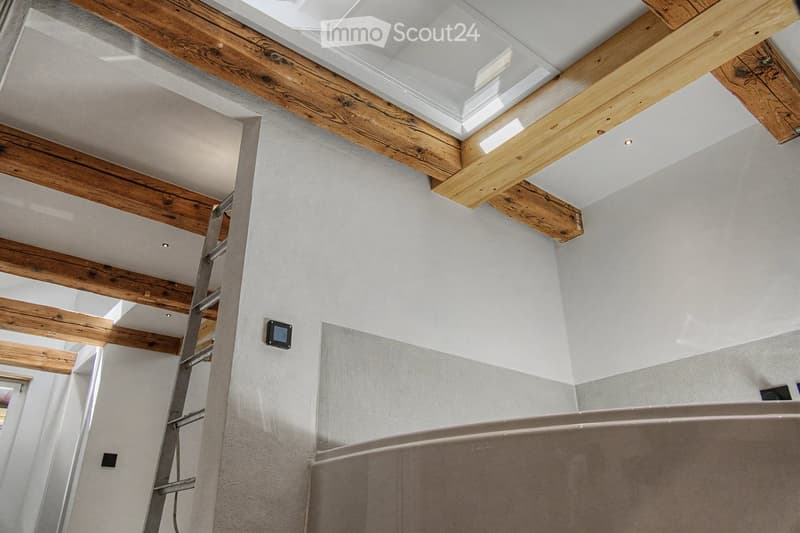 Modern bathroom with exposed wooden beams, skylight, and a large bathtub.