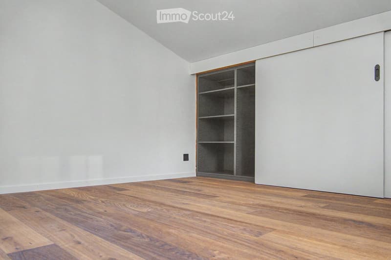 Empty room with light grey walls, wooden floor, and a built-in closet with shelves.