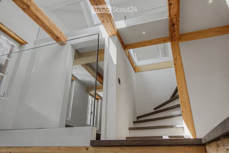 Modern hallway with wooden beams, glass railing, and a staircase leading to an upper level.