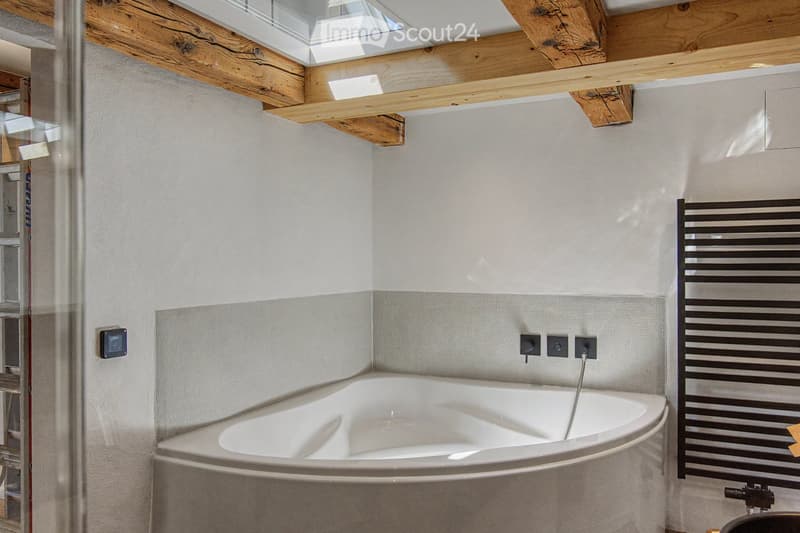Modern bathroom with a corner bathtub, sleek radiator, and exposed wooden beams on the ceiling.