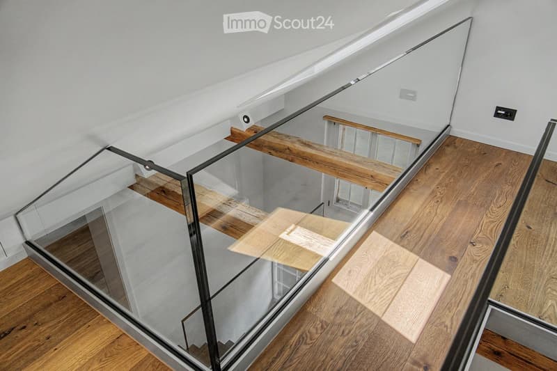 Modern interior staircase with wooden steps and glass railing, leading to an upper level.