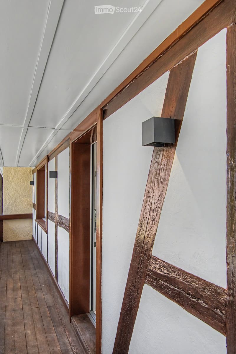 Wooden-floored hallway with white walls, wooden doors, and built-in wooden benches on one side.