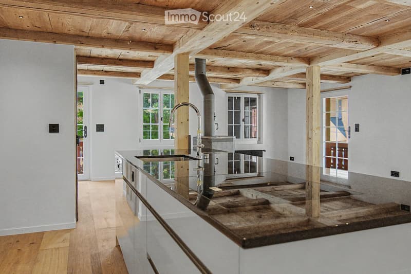 Modern kitchen with wooden beams, a stainless steel sink, and a wooden countertop. The space features large windows and a rustic design.