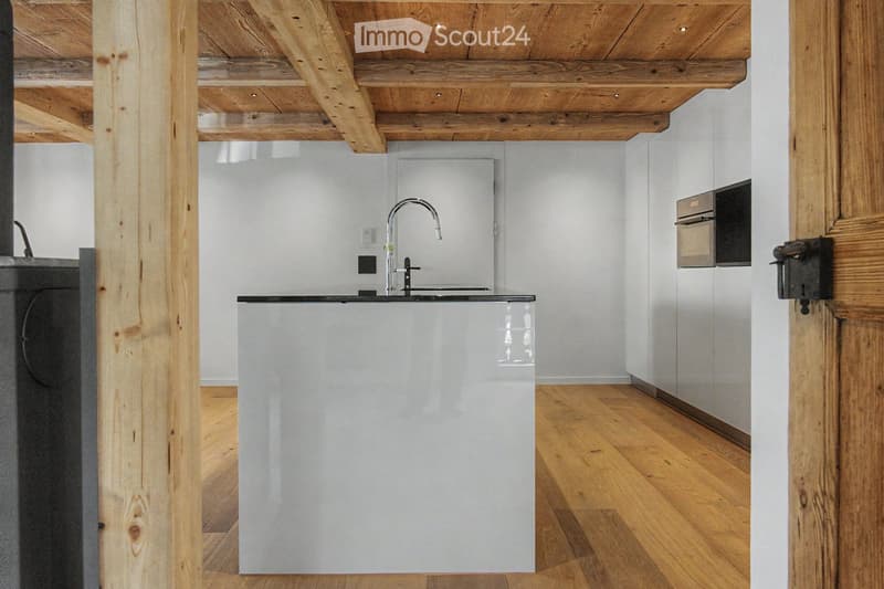 Modern kitchen with white cabinets, wooden ceiling beams, and a sleek black countertop.
