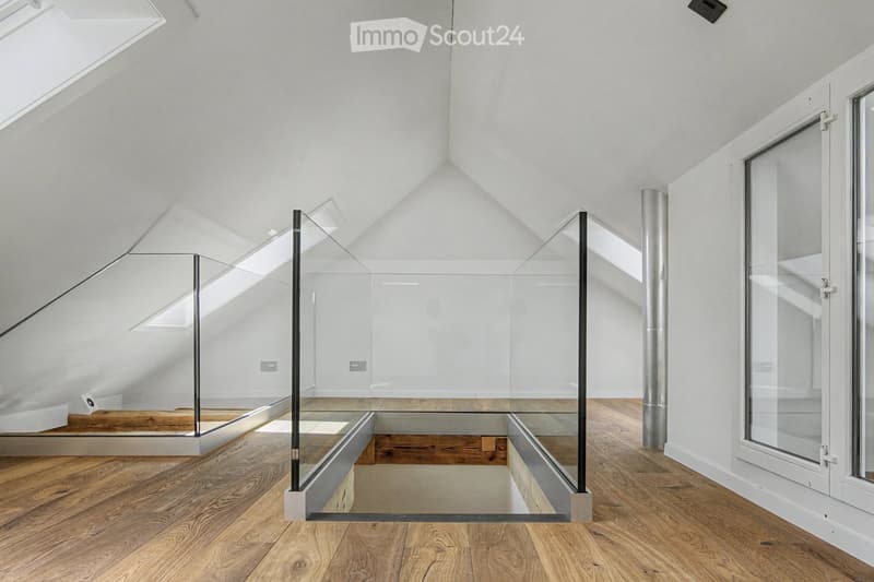 Bright, open hallway with wooden flooring, glass partitions, and skylights allowing natural light to flood the space.