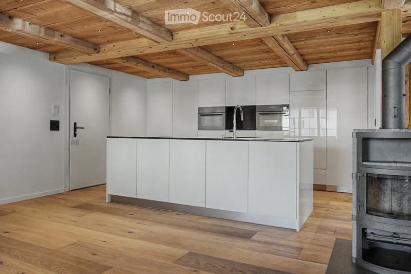 Modern kitchen with white cabinets, a central island, and a built-in oven. Features a wooden ceiling with exposed beams and a wooden floor.