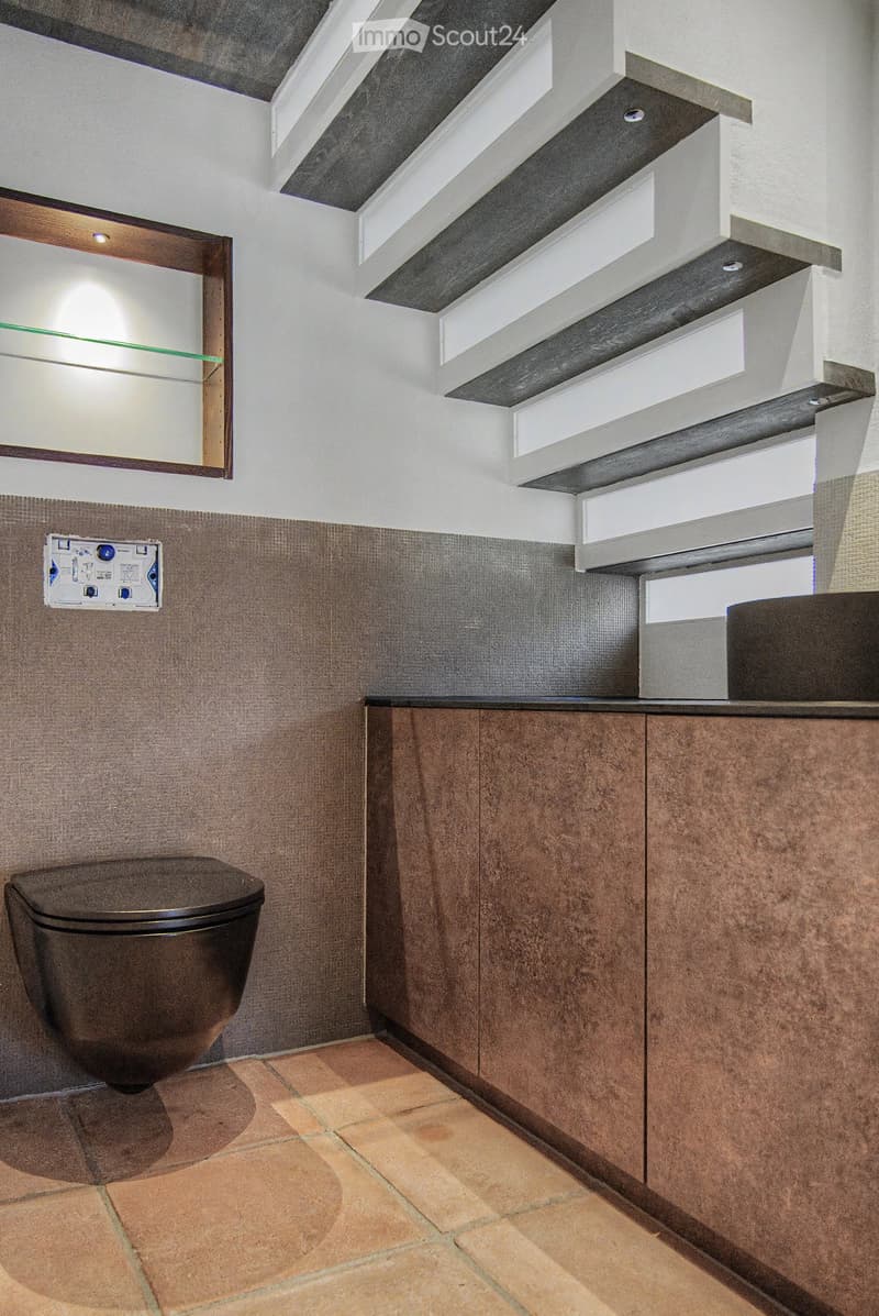 Modern bathroom with a dark brown toilet, wooden cabinets, a mirror with shelves, and a tiled floor.