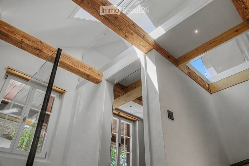 Modern hallway with exposed wooden beams, skylights, and large windows allowing natural light to flood the space.