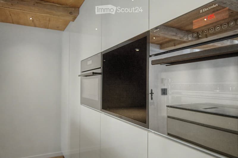 Modern kitchen with white cabinets and a stainless steel oven, featuring sleek design and wooden ceiling.