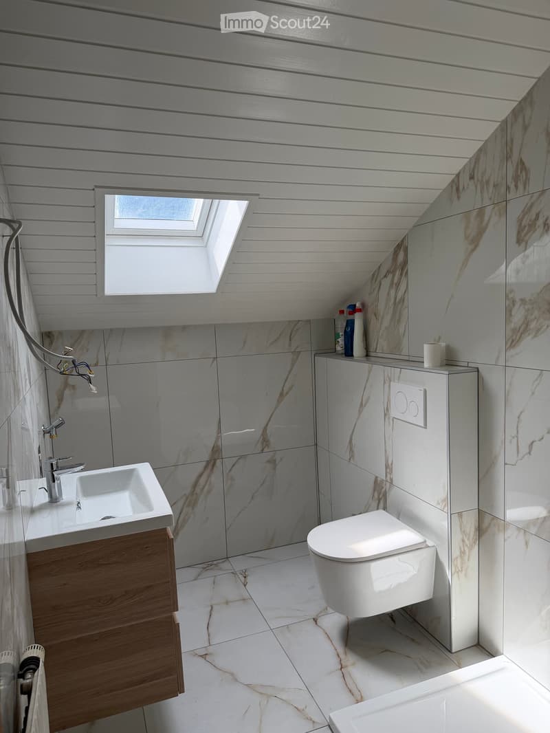 Modern bathroom with white marble tiles, wooden cabinet, sink, toilet, and a skylight window.