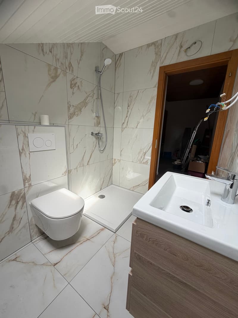 Modern bathroom with white marble tiles, a toilet, a large sink with a wooden cabinet, and a shower area with a glass enclosure.