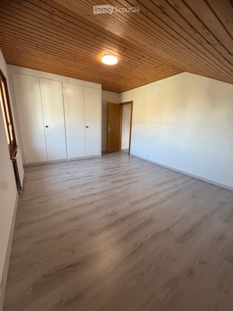 Empty room with wooden flooring, white walls, built-in white closet, and a wooden door leading to another space.