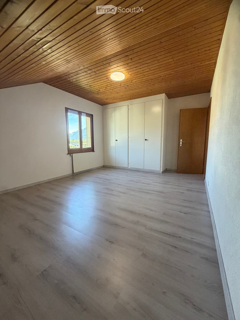 Empty room with wooden flooring, white walls, a large window with a view, white built-in wardrobes, and a wooden door.