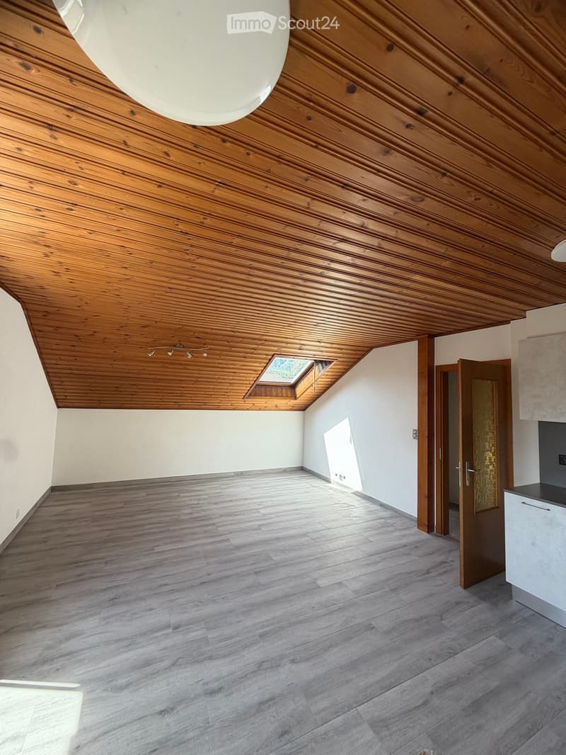 Empty attic space with wooden slatted ceiling, skylight window, and grey wooden flooring.