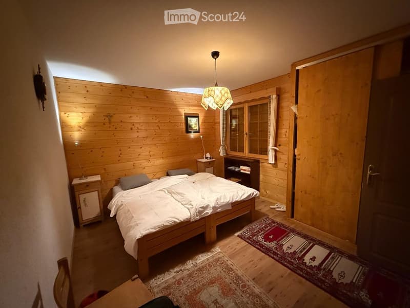 Cozy wooden bedroom with a double bed, nightstands, a mirror, bookshelf, and warm lighting.