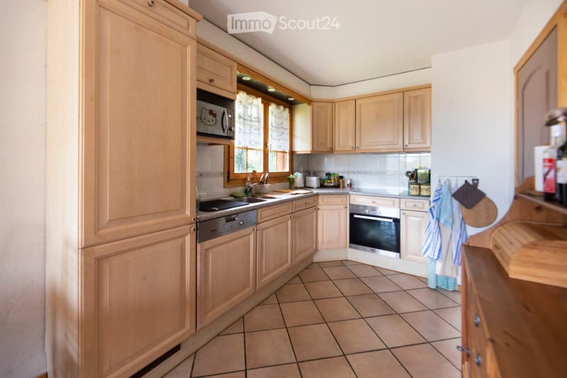 A well-lit kitchen with light wooden cabinets, tiled floor, and stainless steel appliances including an oven, microwave, and sink.