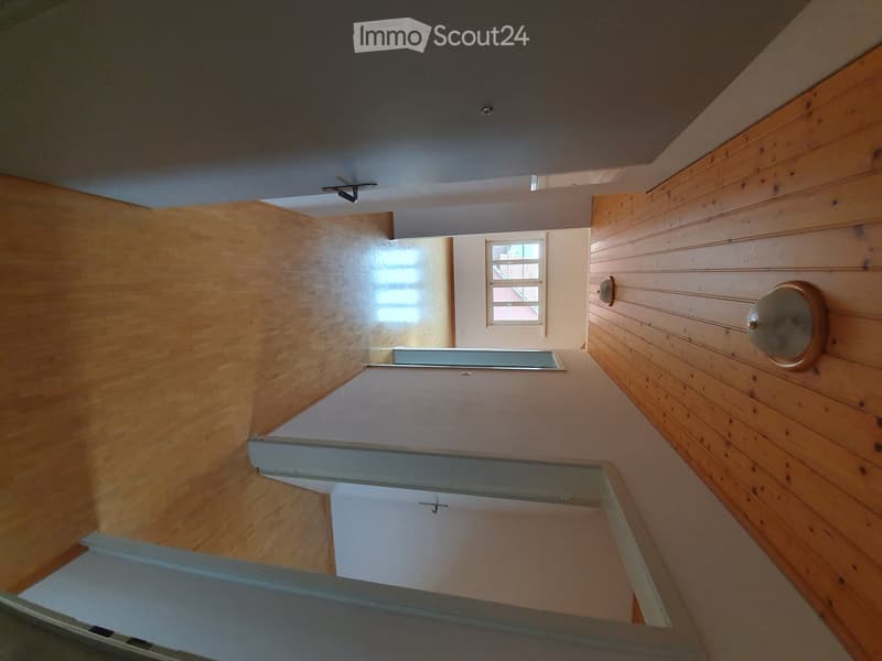 Empty hallway with wooden walls, a small window, and a staircase leading upwards.