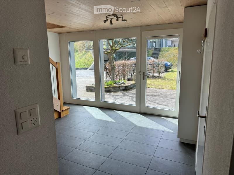 Bright hallway with large sliding glass doors leading to a garden area, tiled floor, wooden ceiling, and modern light fixtures.