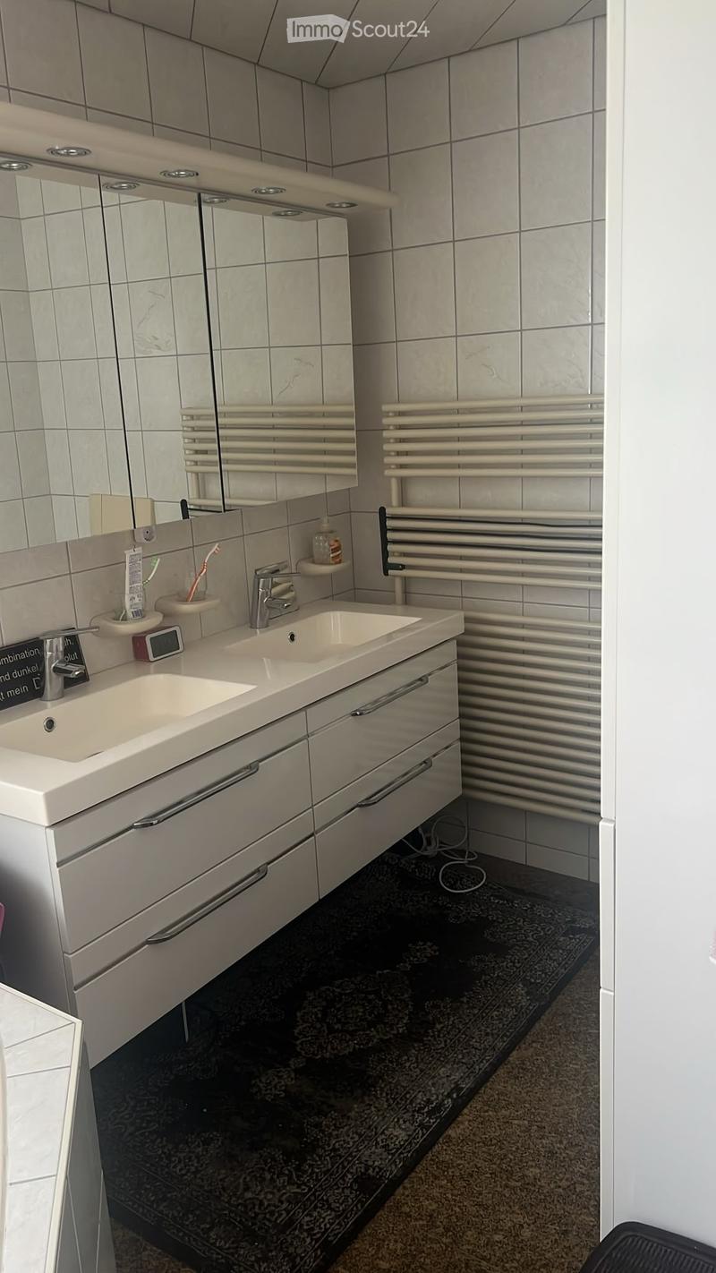 Modern bathroom with a double sink vanity, mirrored cabinet, toothbrush holders, and a radiator. The floor features a dark patterned tile.