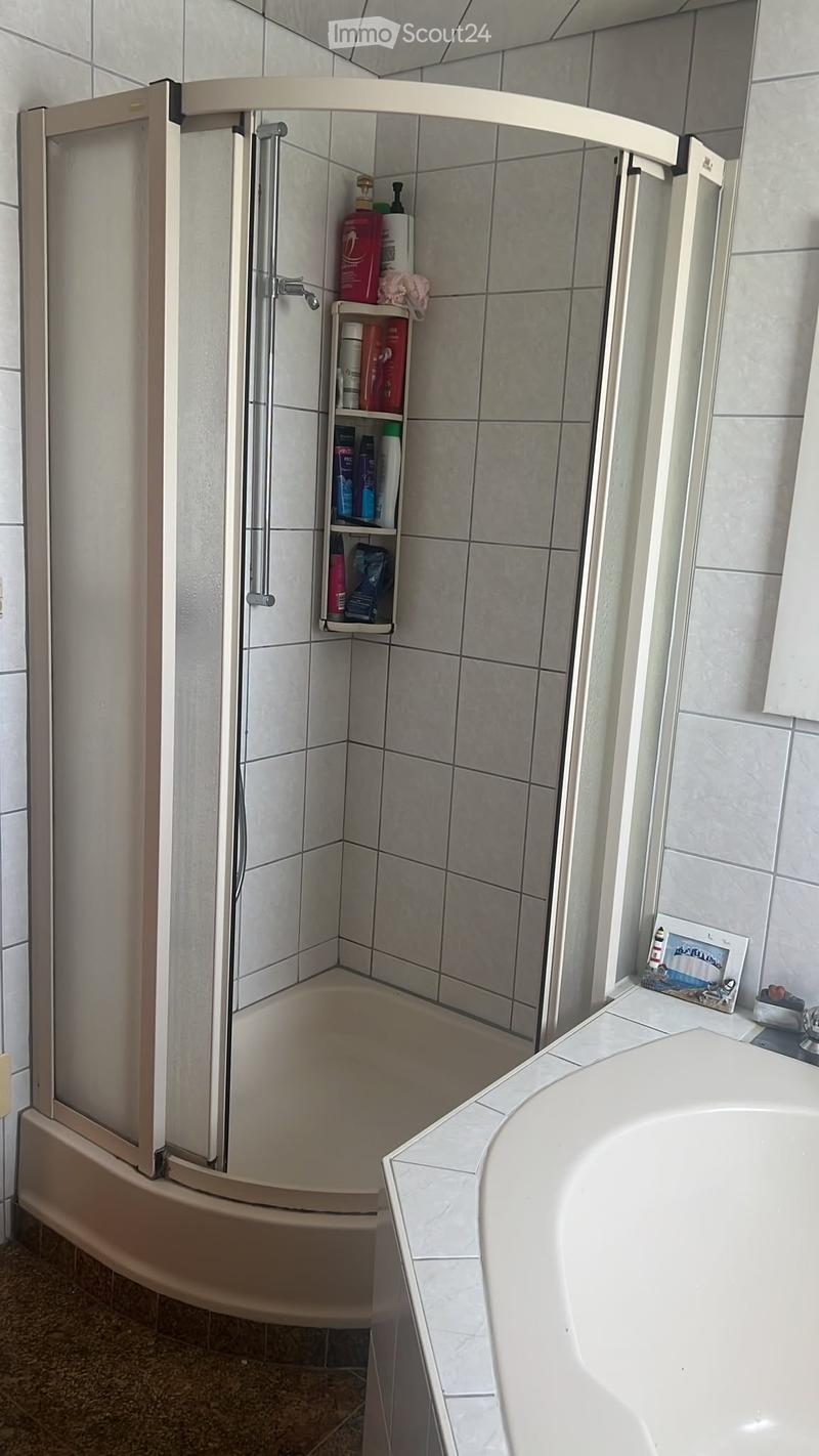 Bathroom with a bathtub, shower stall, and a small shelf holding toiletries. A picture frame is placed on the edge of the bathtub.