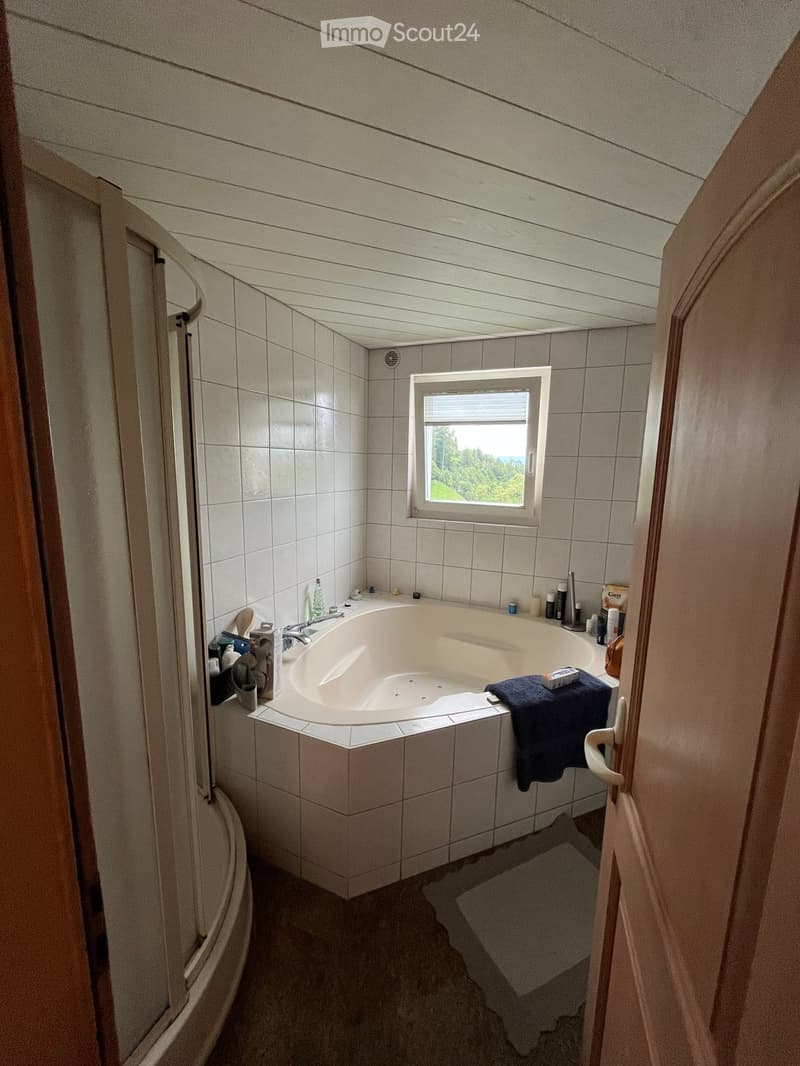 Bathroom with a large bathtub, tiled walls, a window with a view, and various toiletries on the edge of the tub.