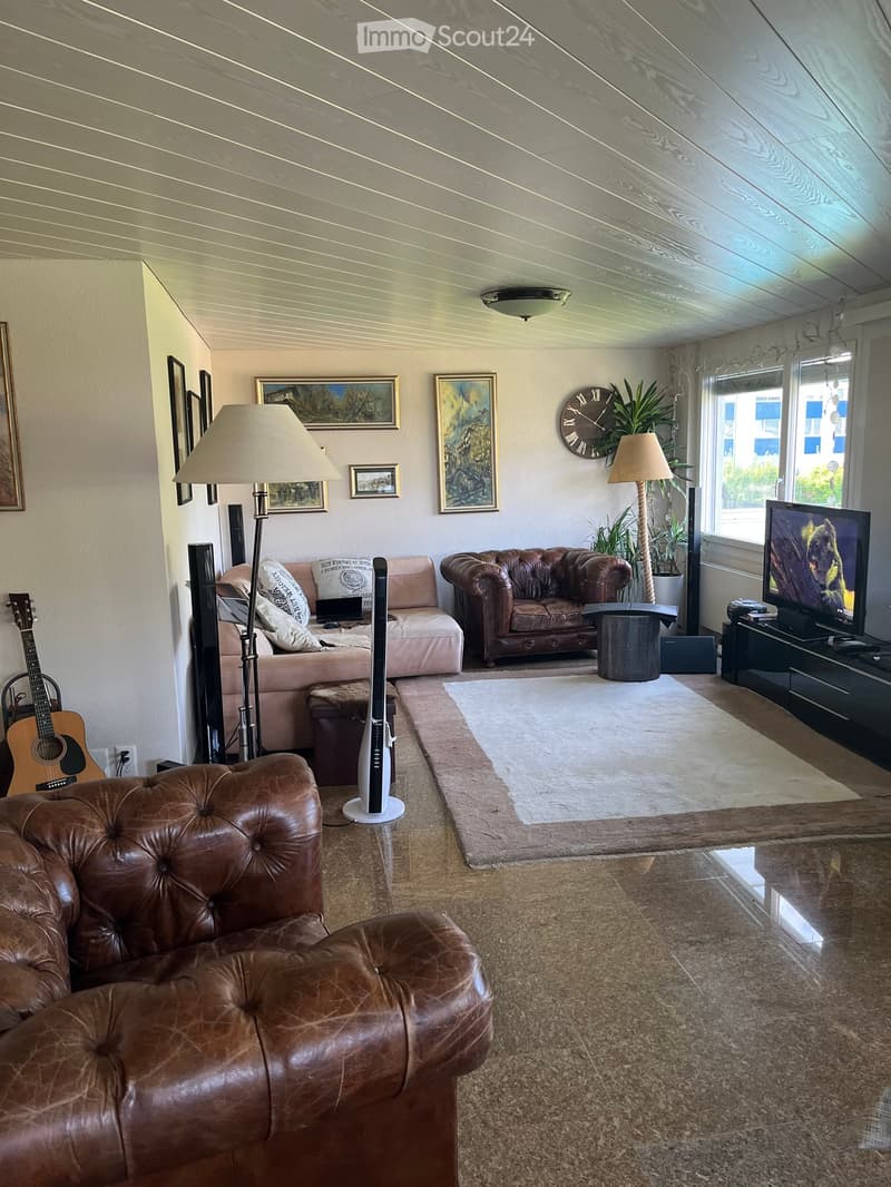 A modern living room with a brown leather sofa, a pink armchair, a coffee table, a floor lamp, a television, and a guitar in the corner.
