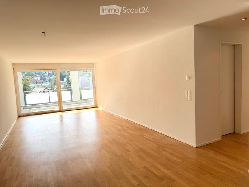 Empty room with wooden flooring, white walls, and large sliding glass doors leading to a balcony.