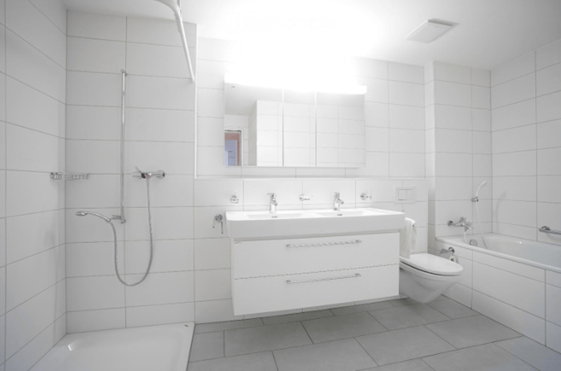 Modern bathroom with white tiles, a double sink, a large mirror, a toilet, a bathtub, and a shower. The space is bright and clean with sleek, contemporary fixtures.