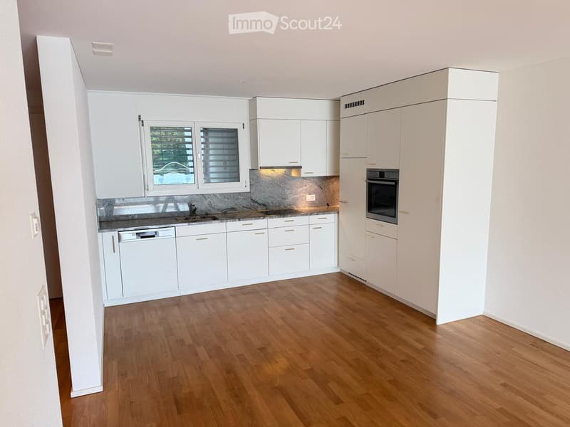 Modern kitchen with white cabinets, wooden flooring, and stainless steel appliances including an oven and dishwasher.