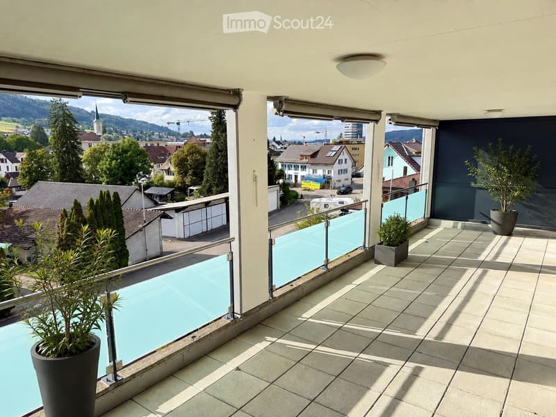 Balcony with tiled floor, glass railing, and scenic city view, featuring potted plants.