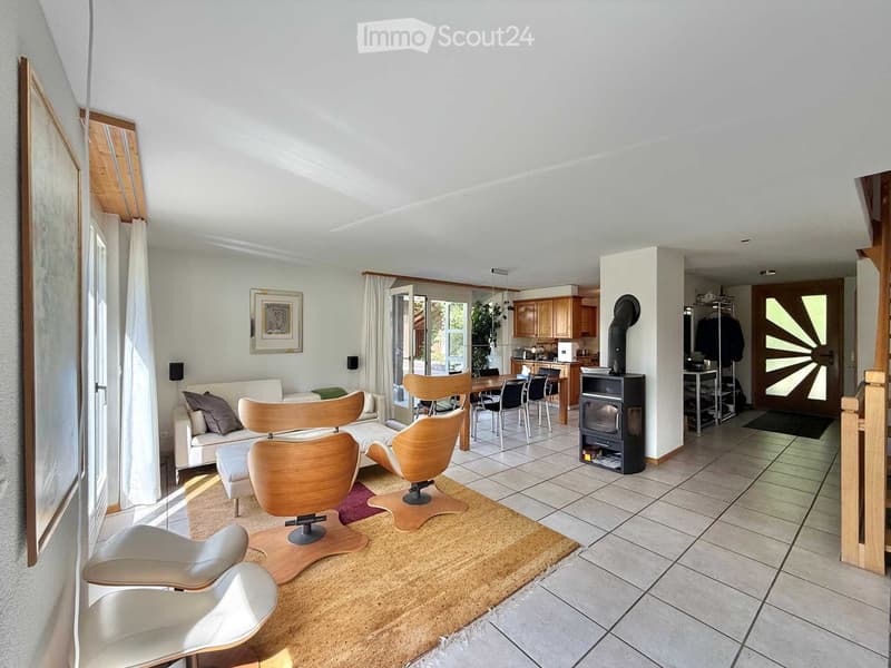 Bright living room with a white sofa, wooden chairs, a fireplace, and a dining area connected to a kitchen with wooden cabinets.