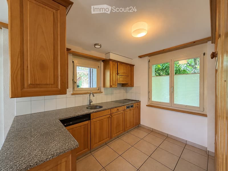 Modern kitchen with wooden cabinets, granite countertop, sink, and dishwasher. Features large windows with blinds and recessed lighting.