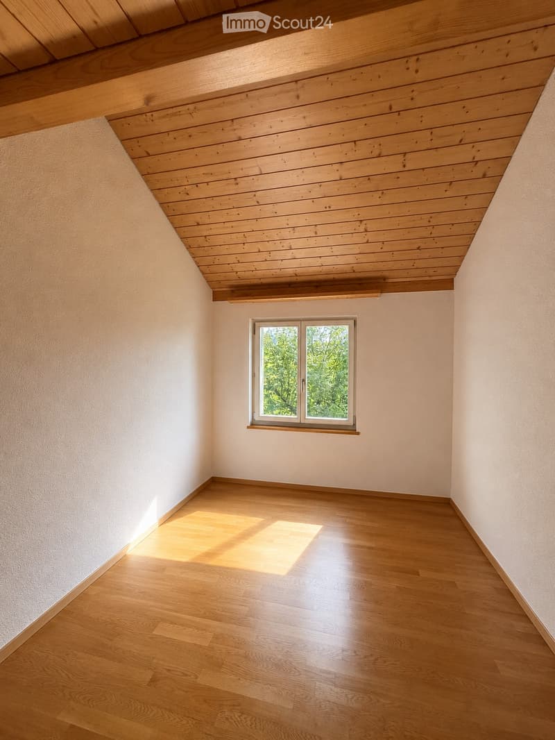 Empty room with wooden floor and slanted wooden ceiling, featuring a single window with white frame and glass panes.