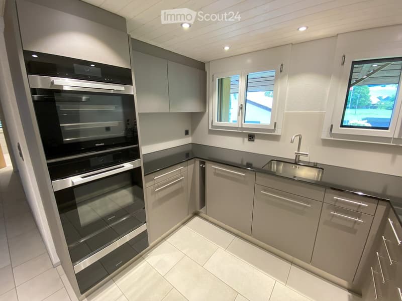 Modern kitchen with grey cabinets, stainless steel appliances, and white tiled flooring.