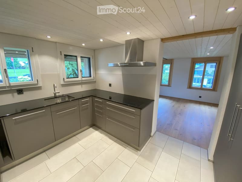 Modern kitchen with grey cabinets, stainless steel sink, and range hood. White tiled floor and light-colored walls.