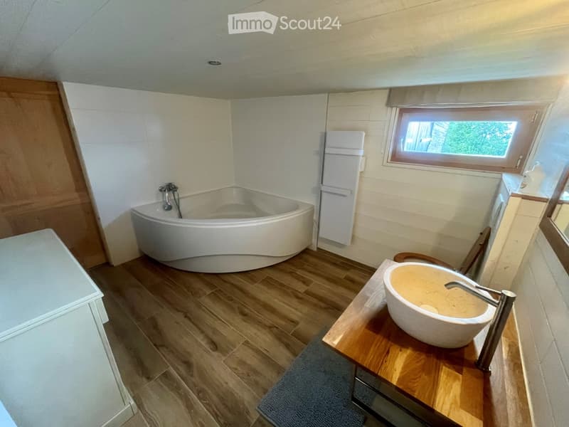Modern bathroom with a curved bathtub, wooden floor, and a sink with a unique bowl-shaped basin on a wooden vanity.