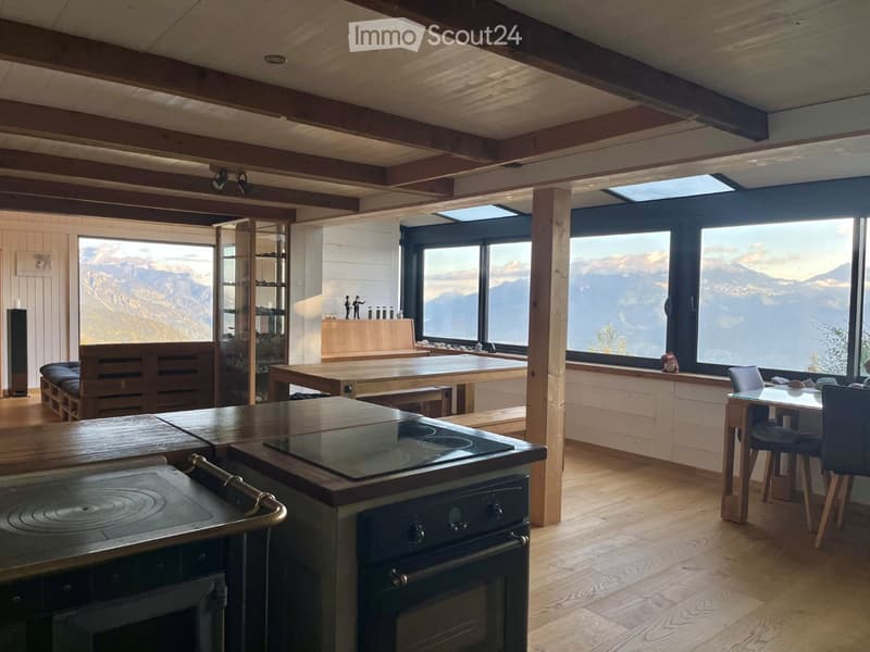 Modern kitchen with wooden beams, large windows offering a mountain view, stove, oven, dining table, chairs, and a bench.
