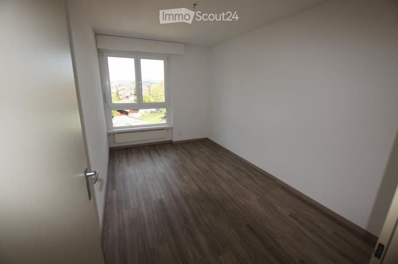 Empty room with wooden flooring, white walls, and a large window with white frame and blinds. No furniture or equipment present.