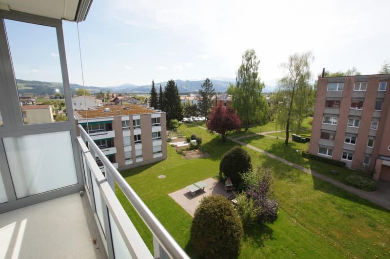 Balcony overlooking a green courtyard with trees, a picnic table, and surrounding buildings.