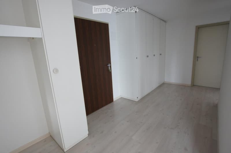 Empty room with light wooden flooring, white walls, built-in white closet, and a wooden door.