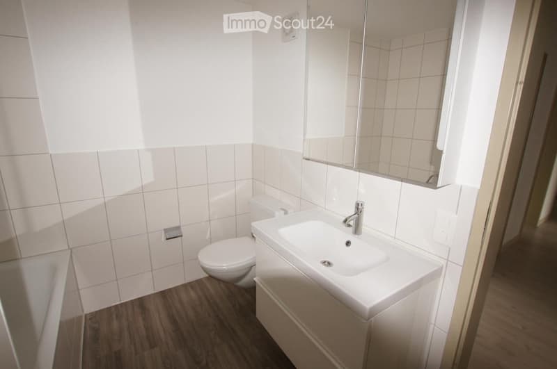 Modern bathroom with white tiles, wooden floor, sink, toilet, and mirror.