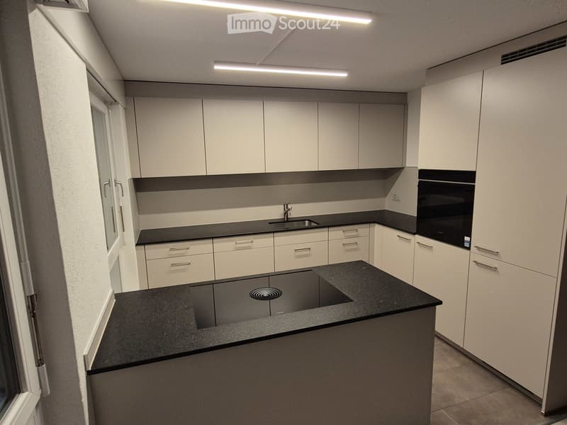 Modern kitchen with white cabinets, black countertops, and built-in appliances including a sink and oven.